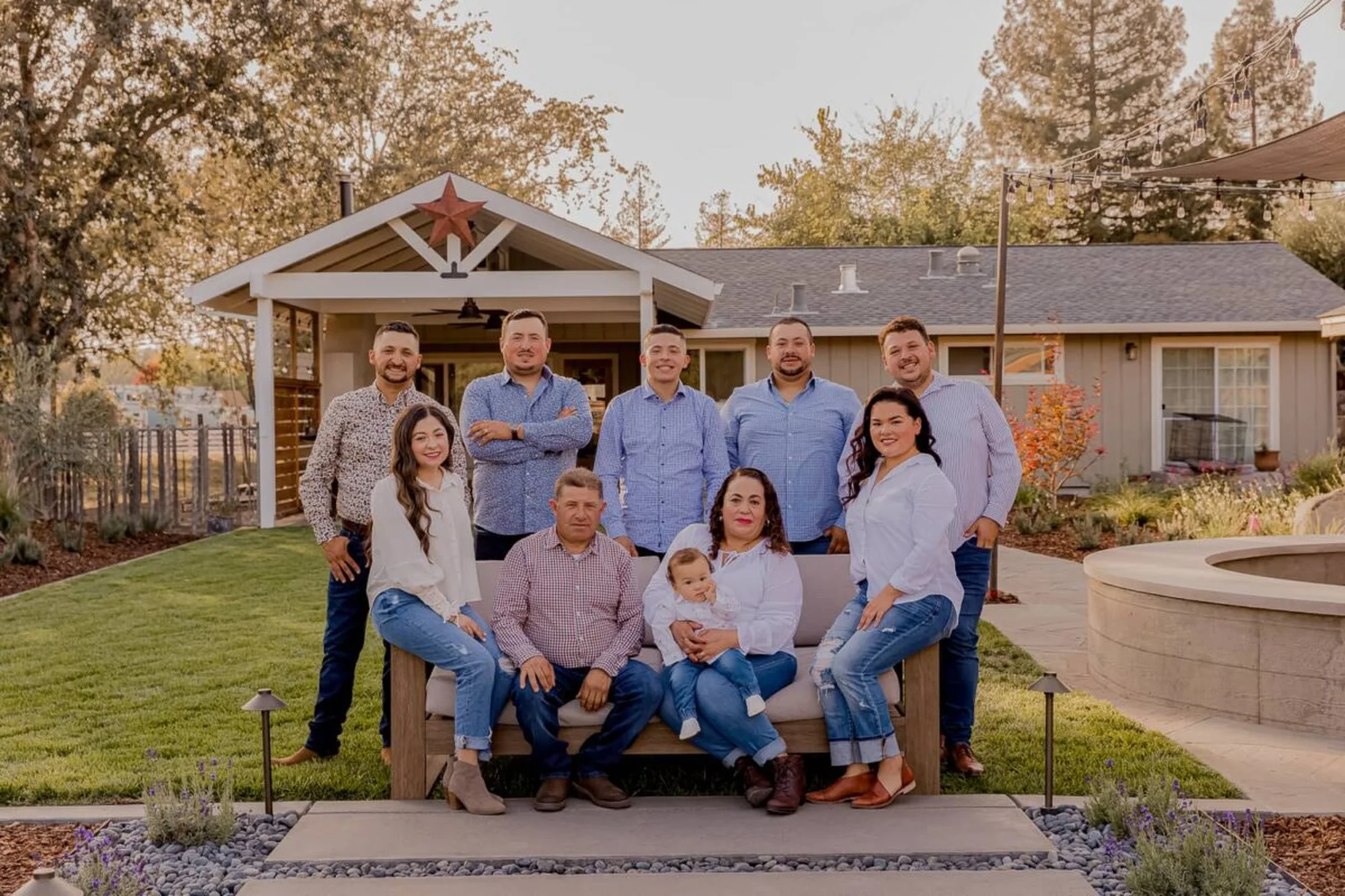 The Highland family seated and standing together in a garden, with a covered patio and string lights behind them