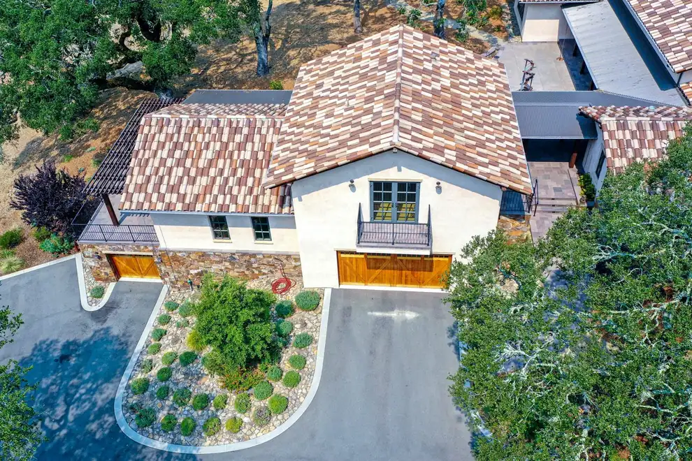 Aerial view of a tile-roofed house with a curved driveway and a river-rock planting bed