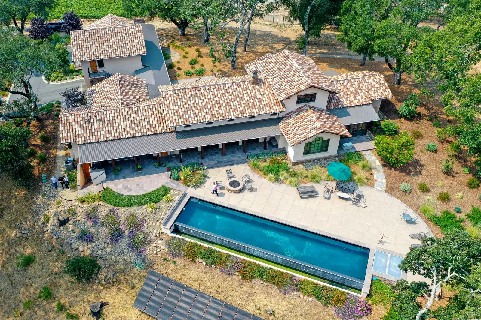 Aerial view of a Sonoma County estate with a long lap pool, stone fire pit, tile-roofed house and oak trees