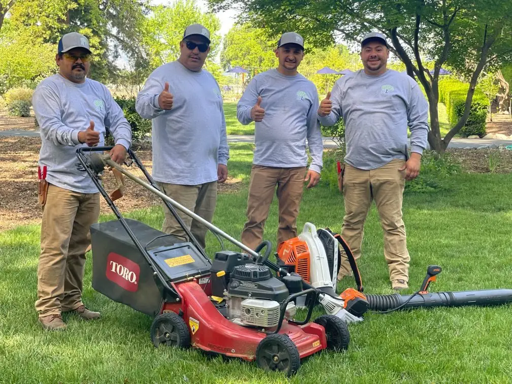 Four Highland crew members giving thumbs up beside a mower and leaf blower