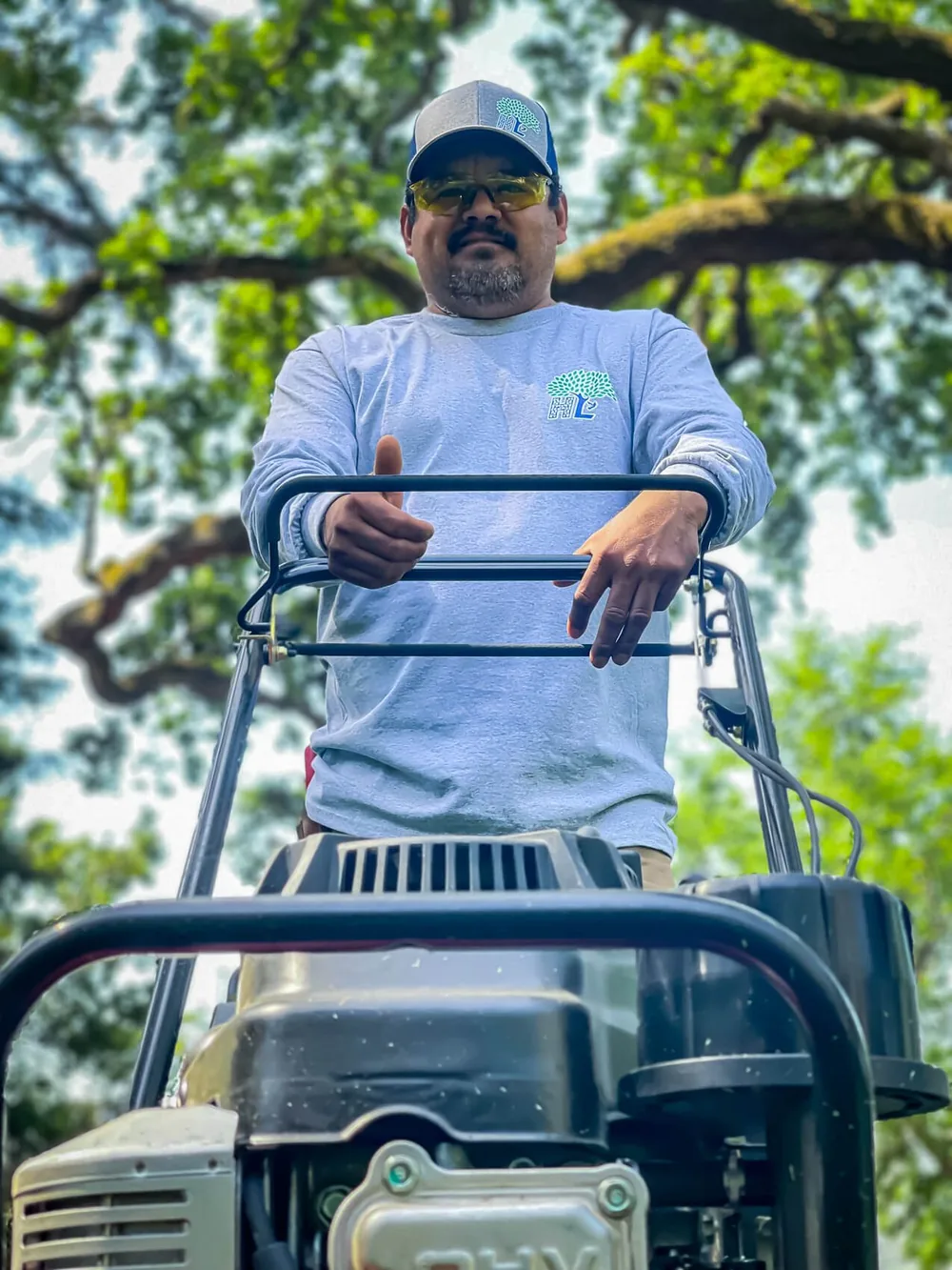 A Highland team member standing behind a lawn mower beneath a large oak