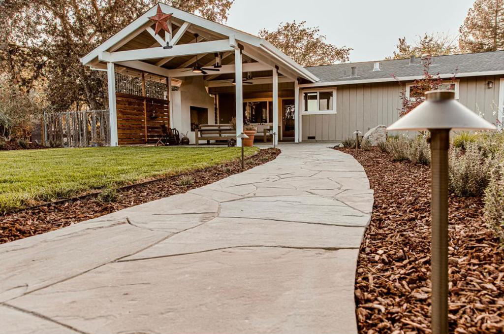 A pergola-covered porch beside a flagstone path lined with landscape lights