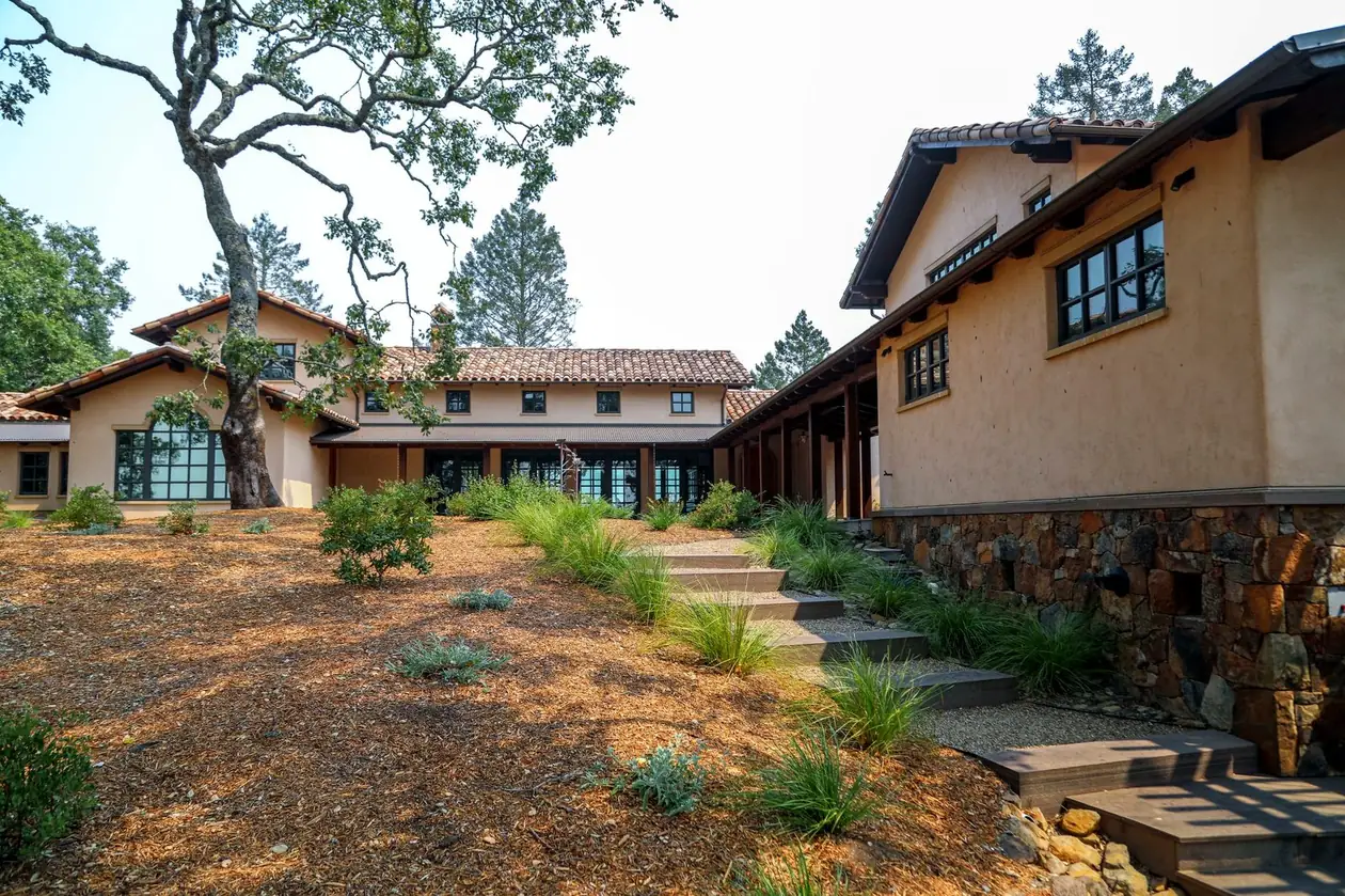 A courtyard of stucco buildings with an oak, gravel path, stone steps and ornamental grasses