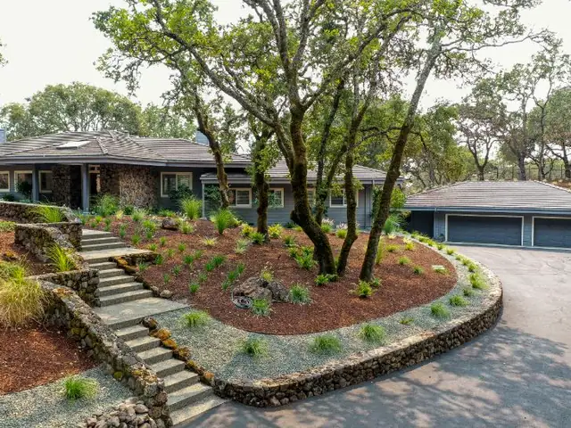 Stacked stone steps and a retaining wall planted with grasses and an oak